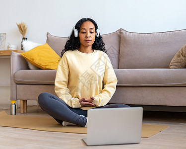 非裔美裔女性在家中用笔记本电脑冥想时 在耳机中监听音乐图片