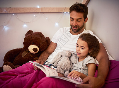 爸爸不先给她读故事 她就睡不着觉 一位父亲在家里和他的小女儿躺在床上看书的镜头图片