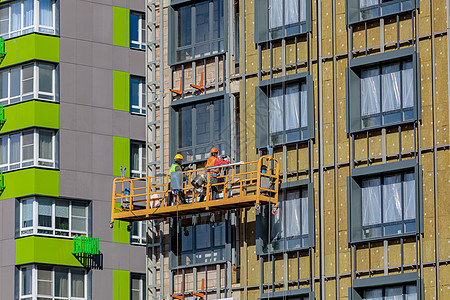 男性建筑工人在一个悬停的摇篮里 在大楼外墙上工作建筑装配工都市墙壁企业绳索安全帽平台高度专业人员图片