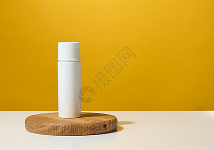 黄色背景的木制讲台上用于化妆品 奶油和液凝胶的白色塑料圆筒图片