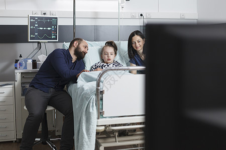 年轻父母和不健康的女儿在儿科诊所看电视 同时坐在小儿科诊所图片