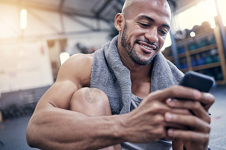 这个应用程序非常适合跟踪我的结果 一个肌肉发达的年轻人在健身房锻炼休息时使用手机的镜头图片