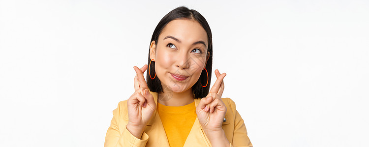 满怀希望的亚洲女孩的特写肖像 她祈祷 交叉手指祈求好运 祈祷和微笑 站在白色背景上快乐学生大学广告女朋友企业家工作室工作办公室标图片