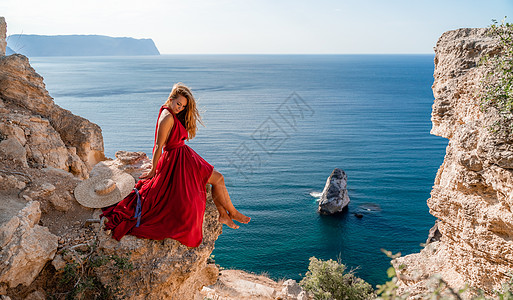 一位身穿红色长裙 头发飘逸的女孩坐在海面上的岩石上 这块石头可以在海中看到成人旅行自由太阳幸福女士丝绸衣服飞行日落图片