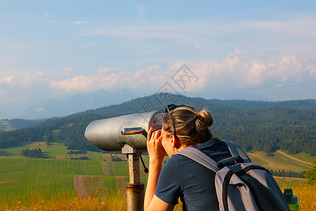女孩透过高山的双筒望远镜看 旅行者图片