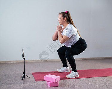 一个胖胖的年轻女子正在看一个在线健身课 在手机上 远程体育培训损失女性班级健身房运动学习腹肌耐力老师讲师图片