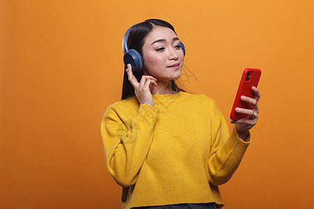 使用智能手机设备 在音频流平台上收听音乐的友好 可爱的亚洲女性(Asian woman)图片