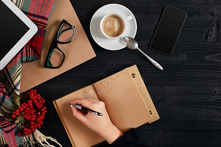 早上 年轻女性右手在木桌上的空白笔记本上写字 旁边放着咖啡杯 智能手机和眼镜办公室职场咖啡店潮人木头日记女士会议作者铅笔图片