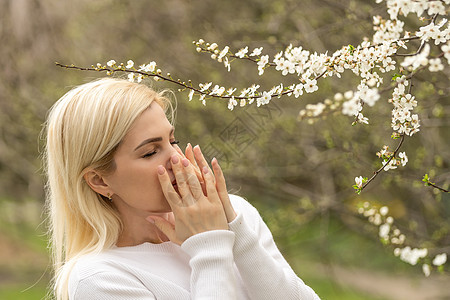 春天患季节性过敏症的妇女过敏 春天在盛开的花园里摆姿势 年轻女子在开花的树前打喷嚏 春季过敏概念背景鼻子女性呼吸药品鼻音花粉公园图片