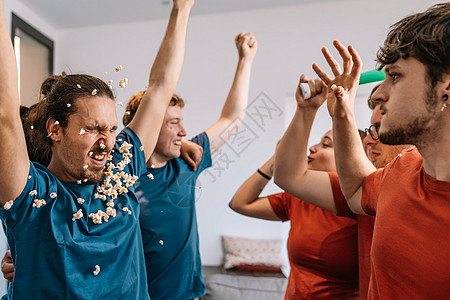 一群朋友在电视上庆祝足球锦标赛 输球的球队向获胜的球队扔爆米花图片
