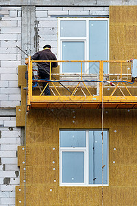 建筑者站在悬浮的平台上 隔绝正在建造的房屋的外墙面图片