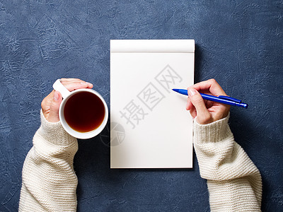 女人用笔记本写在深蓝桌子上 手拿着铅笔 茶杯 草图画的衬衫图片