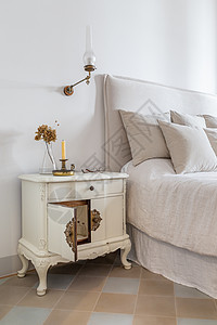 复古风格的舒适房子内部 经典卧室 木制床头柜上放着蜡烛 眼镜和鲜花 床边开着门 靠近舒适的床图片