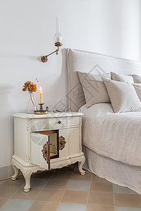 经典的卧室 在靠近舒适床的木制床头柜上放着燃烧的蜡烛 眼镜和鲜花 复古风格的舒适房子内部图片