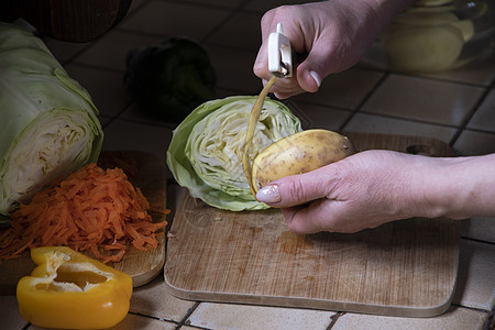 一名妇女以新鲜蔬菜为背景 在厨房里剥土豆皮骰子厨师皮肤美食木板土豆女士烹饪收成洋葱图片