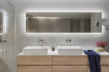 现代浴室内有木架 两个白色水槽和大镜子 深蓝色毛巾和装饰用的鲜花图片