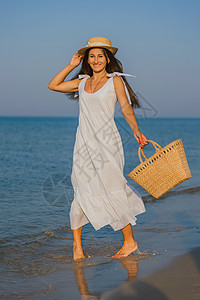 在沙滩上戴帽子的女人编织热带蓝色金发柳条篮子女士闲暇海岸海洋图片