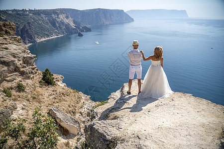 新人站好 新娘已将手搭在新郎的肩上 望着Fiolent美丽的海景 新娘穿着婚纱 新郎穿着白衬衫 短裤 帽子图片