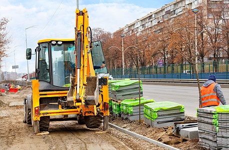 一家橙色公路挖土机在春季下午沿城市街道铺设铺路板的工地施工图片