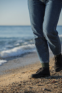 穿蓝色牛仔裤和黑鞋的女子在海滩上行走 背景是海浪图片
