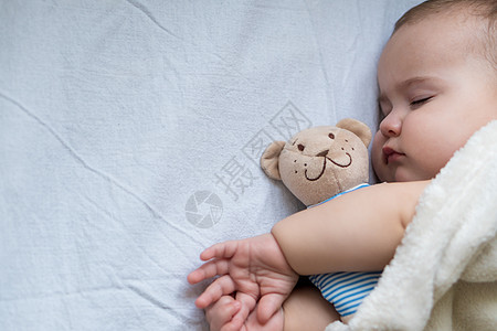 童年 护理 母性 健康概念  特写小和平平静的婴儿蹒跚学步的女婴睡觉休息深睡在柔软温暖的毯子上拥抱泰迪熊玩具 闭上眼睛躺在大床上图片