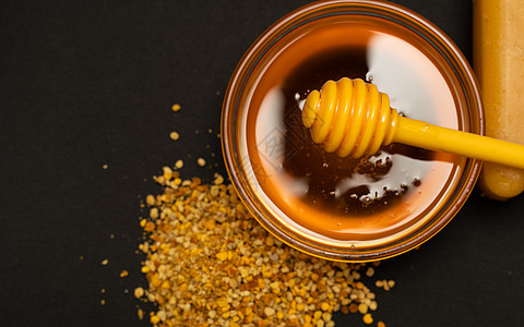 一勺黄色蜂蜜浸在一罐蜂蜜和散落在黑色背景上的蜂面包中 亲爱的四处滴水 漂亮而诱人的照片 健康食品的概念摄影核桃木头食物蜜蜂美食花图片