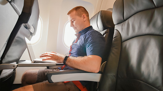 一名青年男子坐在飞机上 在出发前正在笔记本电脑上工作图片