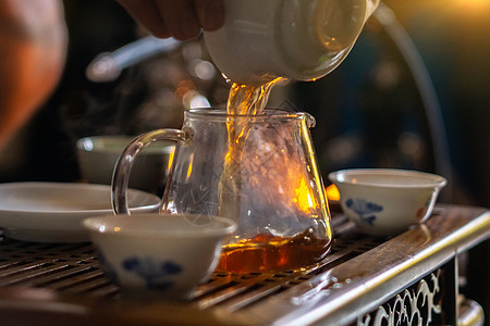 一只把中国茶水从玻璃茶壶倒进小杯子的手图片