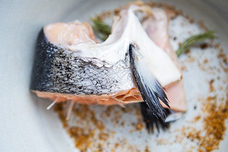 一块被切开的鲑鱼牛排和香料和迷迭香放在盘子上图片