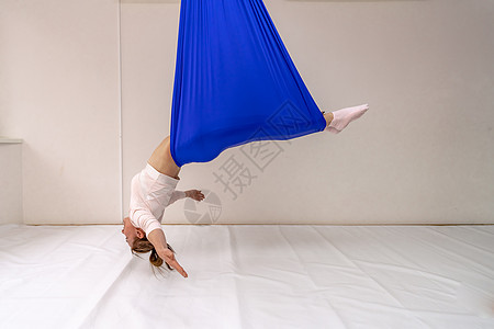 一名年轻女子在白色背景的蓝吊床上做反重力空中瑜伽时摆姿势力量健身房天线运动福利成人女性吊床航空女士图片