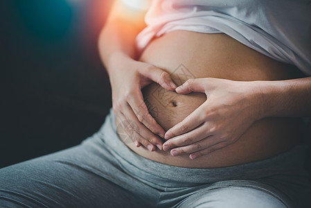 孕妇在家中的肚子上握着心脏形状的手 怀孕妇女用双手做心 闭紧图片