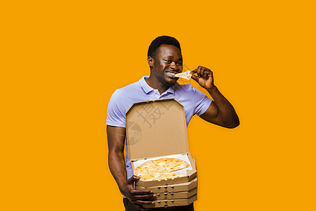 有趣的黑色快递员吃着一块披萨 拿着 4 个披萨盒 从餐厅送来美味的比萨饼 披萨配奶酪板广告图片