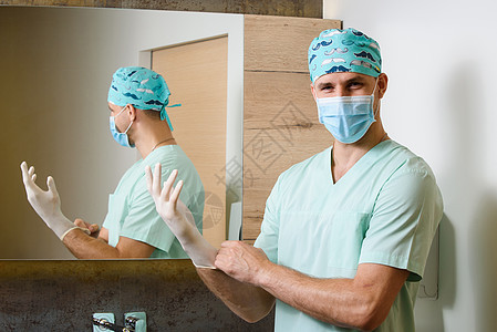 微笑外科医生将无菌的医用手套戴在手上 并秘密地看 保护大流行的 Corona病毒为19个人提供卫生服务图片