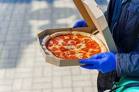 餐饮安全比萨饼 带医用手套的食品运送人 配奶酪和沙拉米的披萨单独照片 停止流行性冠状病毒共食19图片