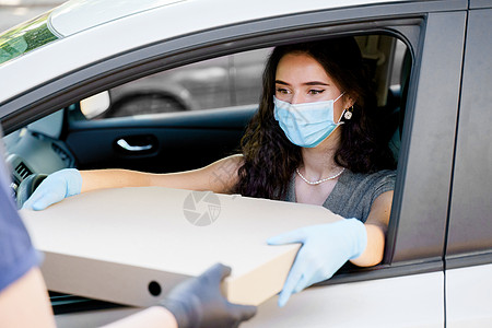 戴着医用口罩和手套的女孩在车里得到了巨大的披萨 纸箱生态盒中的大尺寸披萨 快递给年轻的女商务人士大比萨饼 汽车送货盒子安全远程人图片