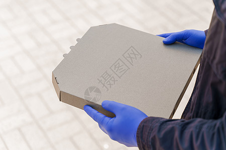 一个纸板比萨盒在信使手中 用蓝晶状的药手套阻止19号科罗纳病毒 呆在家里图片