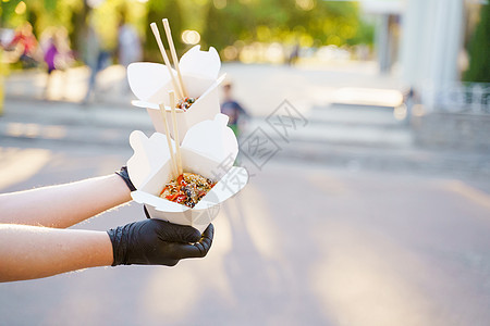 特写美味的食物炒锅在盒子交付 男人戴着黑色医用手套 用筷子夹着乌冬面 一次性生态盒中的中国辛辣食品广告饭盒美食外卖午餐面条拉面蔬图片