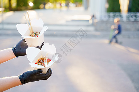 特写美味的食物炒锅在盒子交付 男人戴着黑色医用手套 用筷子夹着乌冬面 一次性生态盒中的中国辛辣食品美食饮食外卖拉面女士午餐营图片