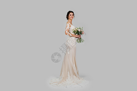 年轻有魅力的新娘 带着鲜花 在现代婚纱外表 帽袖和幻想领带顶部 从柱子周光和扫铁列上花束花朵女士成人裙子工作室婚礼订婚奢华女性图片