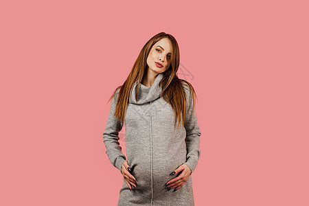 一个穿着粉红色背景灰色毛衣的快乐漂亮女孩怀孕了 怀孕的女人 孩子的期望 产假女性肚子微笑母性腹部粉色福利分娩女士母亲图片