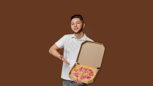 英俊的年轻快递员微笑并指向披萨 空空间做广告宣传 在现场张贴广告和海报;从餐馆到网上提供比萨安全服务图片