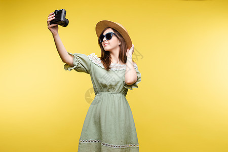 快乐的女旅行者假扮自拍 使用在黄色工作室背景上隔离的相机图片