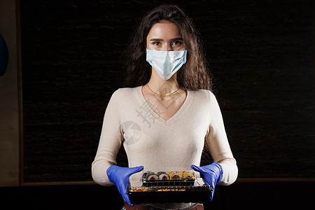 有寿司的女孩 戴着医用面具的食品快递员 在检疫冠状病毒 covid19 交付 年轻女子戴着手套手里拿着 2 个寿司盒盒子餐厅大豆图片