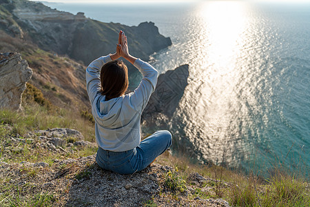 女性游客享受海山地貌的日落 坐在海面上的岩石上户外 穿着牛仔裤和蓝色连帽衫 健康生活方式 和谐与冥想 续海洋手势旅行手印天空喜悦图片