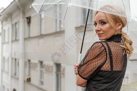 金发女郎在下雨时站在透明伞下 秋季 后视线 女人穿着黑色的蕾丝裙 头发被马尾巴拉回来 笑声秘书正装企业家卷曲情感发型商务人士工人图片