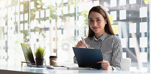 年轻亚洲女商务人士在现代办公室用平板电脑作笔记 看镜头 (笑声)图片