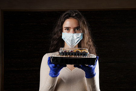 有寿司的女孩 戴着医用面具的食品快递员 在检疫冠状病毒 covid19 交付 年轻女子戴着手套手里拿着 2 个寿司盒塑料大豆盒子图片
