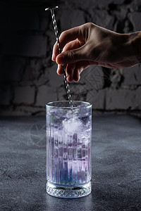 鸡尾酒在一个高大的杯子里 有蓝色的液化和冰 装饰着灰色背景的白花图片