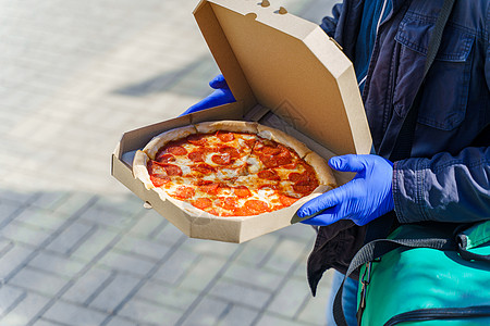 餐具盒中带沙拉米和奶酪的比萨饼 餐厅用蓝色医疗手套安全送货 冷冻冠状病毒(19)检疫图片