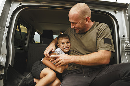 快乐的父亲和儿子坐在汽车后备箱里冒险男生旅行车辆公园树干运输农村男人喜悦图片